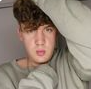 Porträt eines jungen Mannes mit lockigem Haar und grauem Pullover – lässige Pose mit direktem Blick in die Kamera