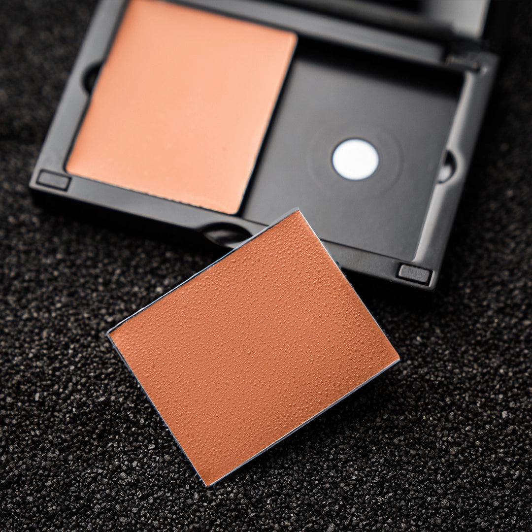 Nahaufnahme eines Concealer-Nachfüllpuders in einem schwarzen Make-up-Behälter auf einer strukturierten Oberfläche – hochwertige Kosmetik für eine gleichmäßige Hautabdeckung