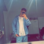Spiegel-Selfie eines jungen Mannes in einem stylischen blauen Outfit mit weißem Shirt – lässige Pose in modern eingerichtetem Zimmer