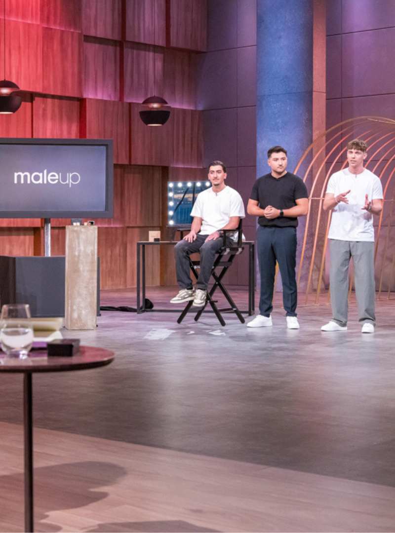 Präsentation von MaleUp in der TV-Show „Die Höhle der Löwen“ – Gründer demonstriert die Anwendung des Concealers auf einem Model, während ein weiterer Teammitglied auf der Bühne steht. Im Hintergrund ist das MaleUp-Logo auf einem Bildschirm zu sehen